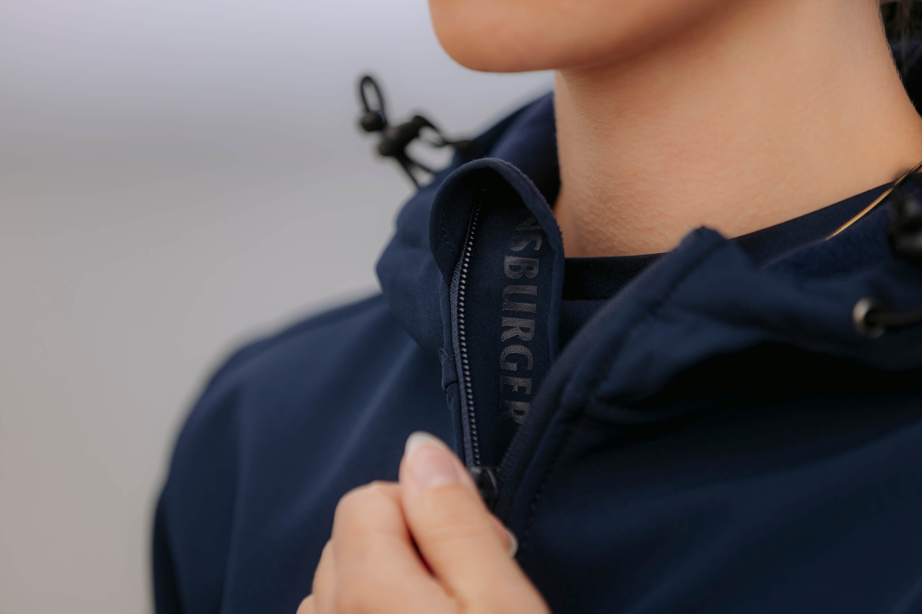 Eine Frau schließt den Reißverschluss ihrer navyblauen Softshelljacke. Innen am Reißverschluss ist der Schriftzug "FLENSBURGER" sichtbar.