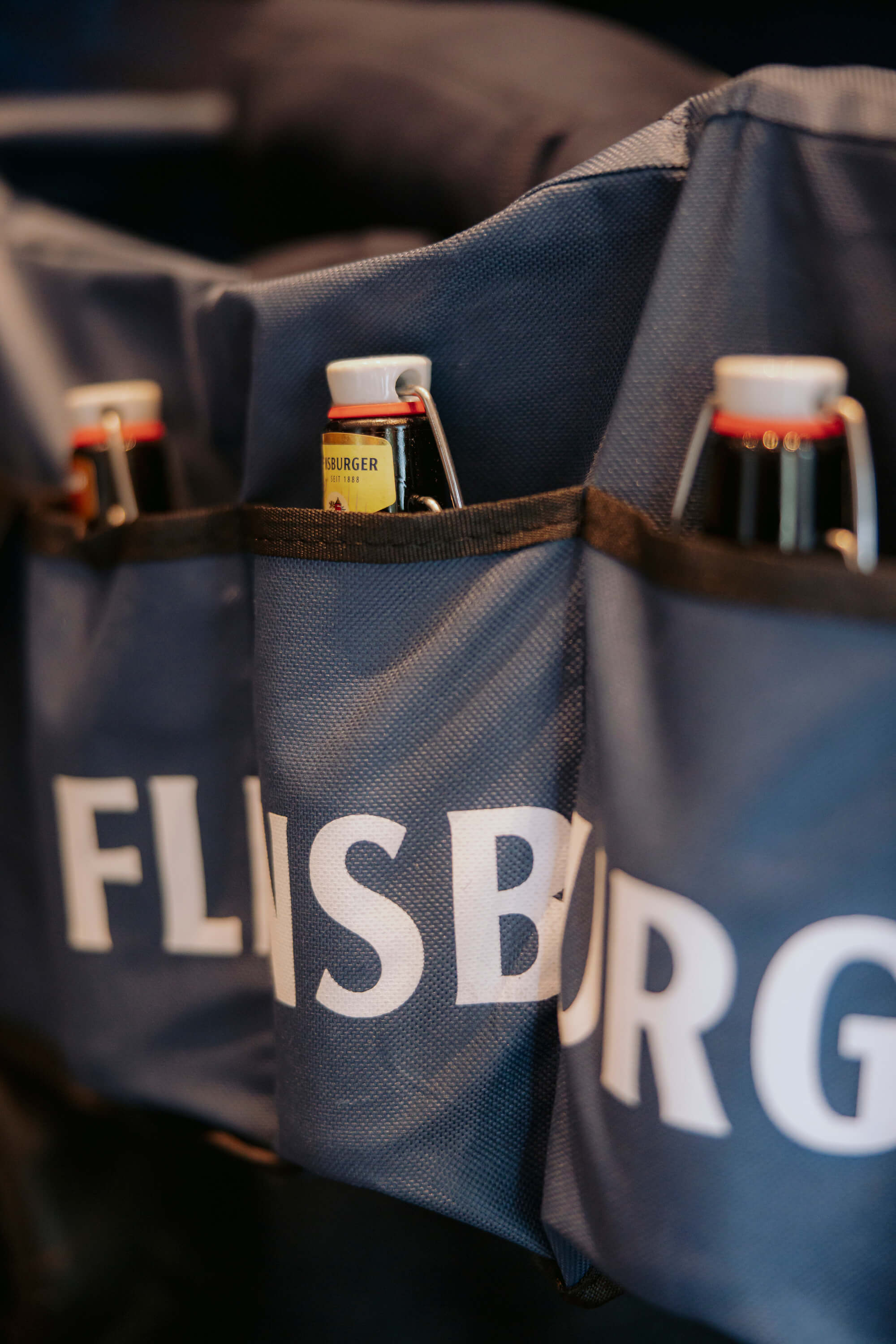 Detailaufnahme zeigt drei Flaschen mit Bügelverschluss, die in den Taschen eines blauen, faltbaren Bollerwagens der Marke Flensburger stecken.