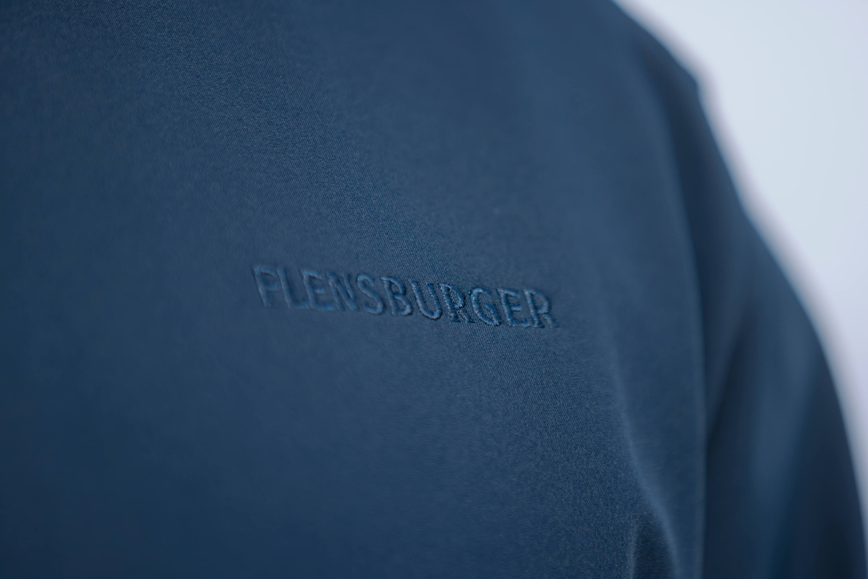 Der Schriftzug „FLENSBURGER“ ist dezent und ton-in-ton auf der blauen Softshelljacke eingestickt.