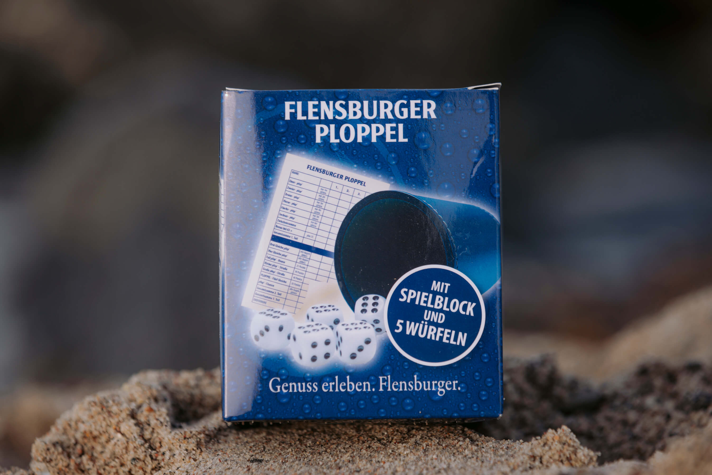 Das Würfelset Flensburger Ploppel zeigt fünf weiße Würfel, einen Spielblock und einen schwarzen Becher. Auf der Verpackung steht: „Mit Spielblock und 5 Würfeln“.