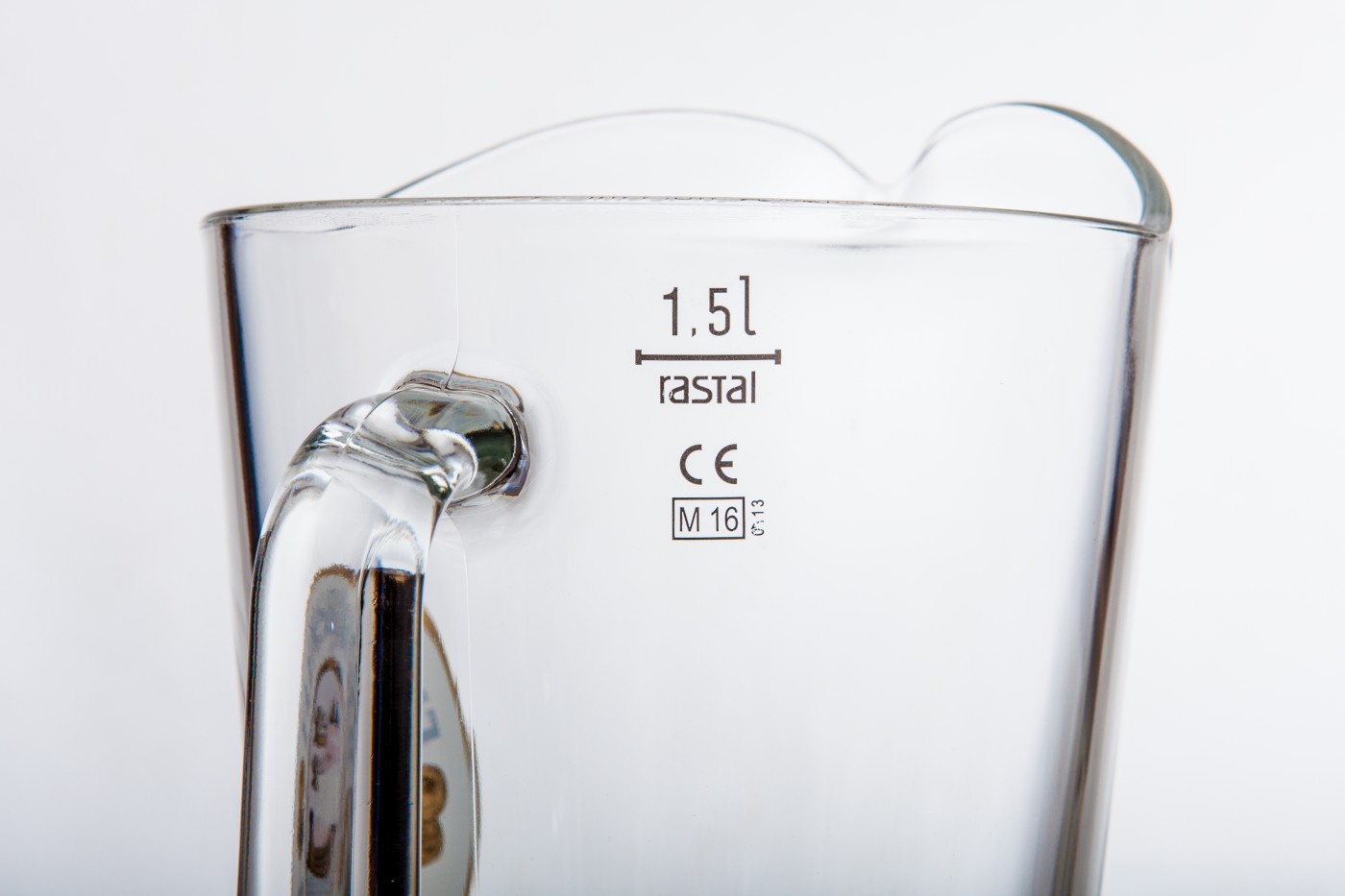 Detailansicht: Glaspitcher aus transparentem Glas mit Henkel. Auf der Oberfläche steht „1,5 l“, „rastal“, „CE“, „M 16“ und „v 13“ in schwarzer Schrift gedruckt.